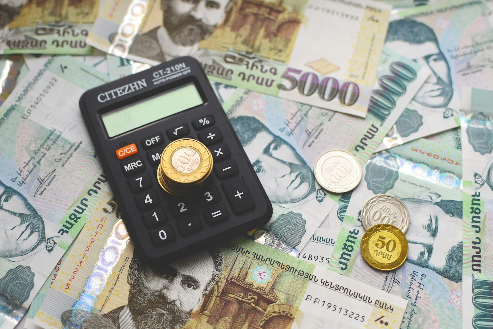 Calculator resting on stacked paper currency next to coins