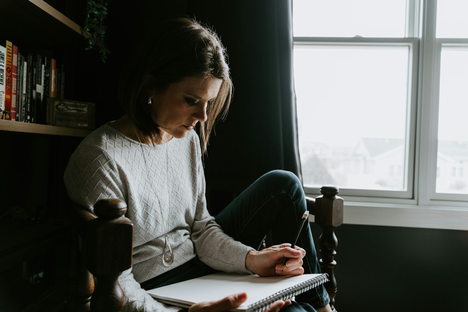 Woman sitting in a chair, journaling with a pen in a quiet room