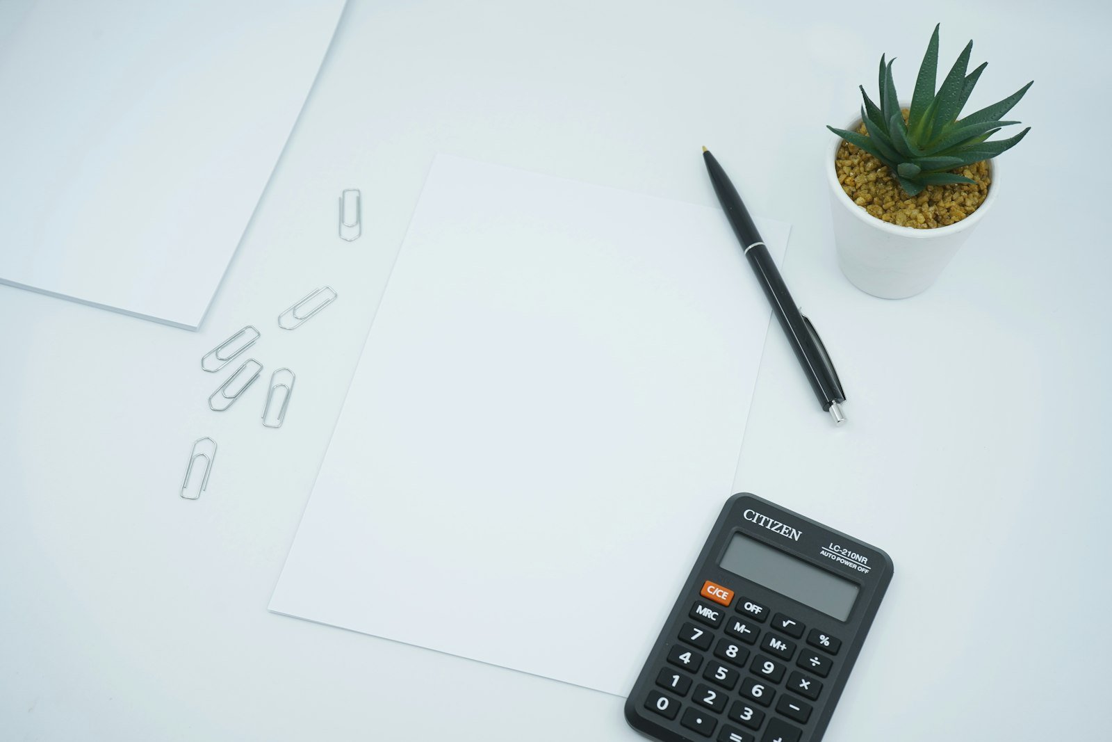 Black calculator next to a black pen on plain white printer paper