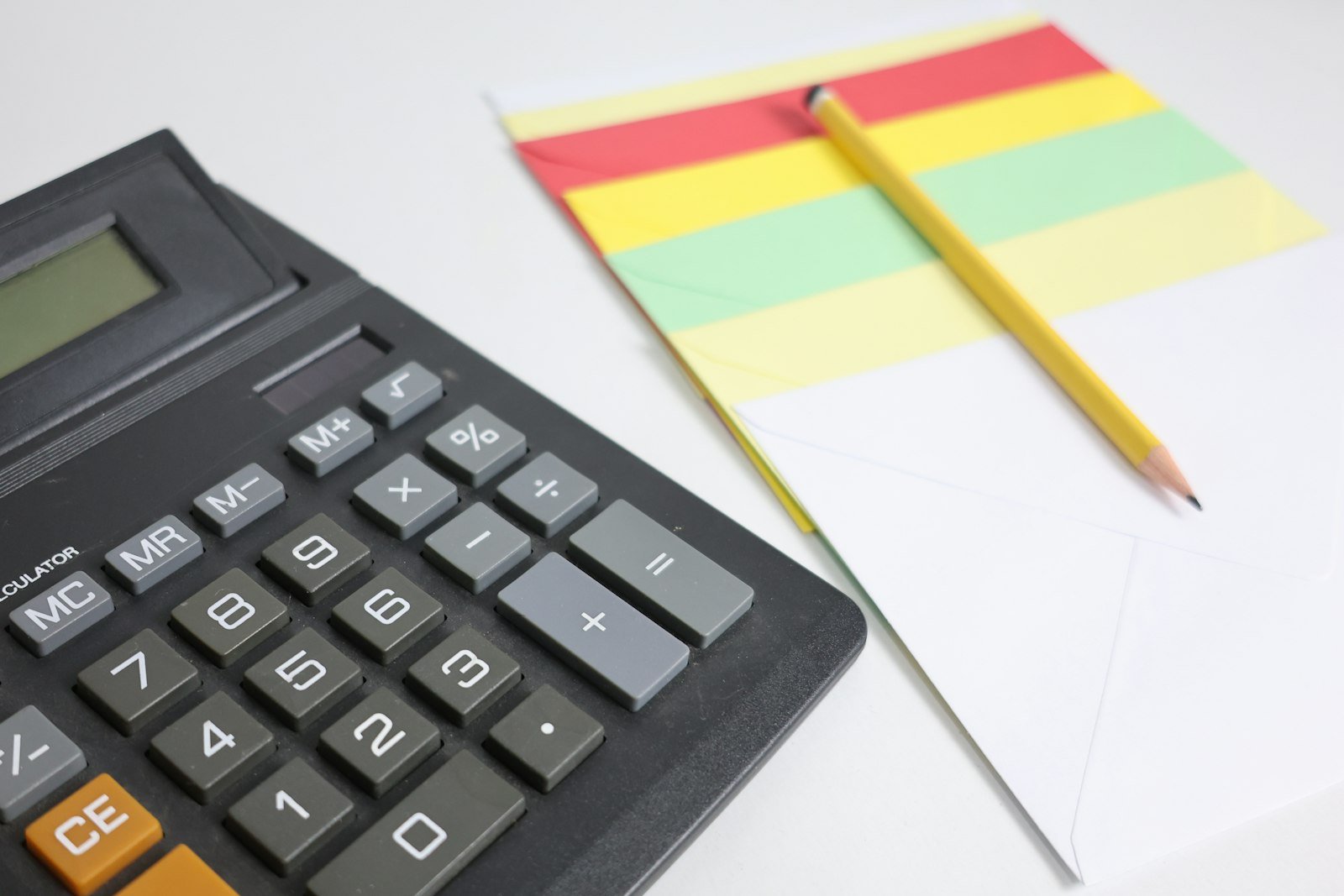 Calculator and notepad with a pencil arranged on a white surface