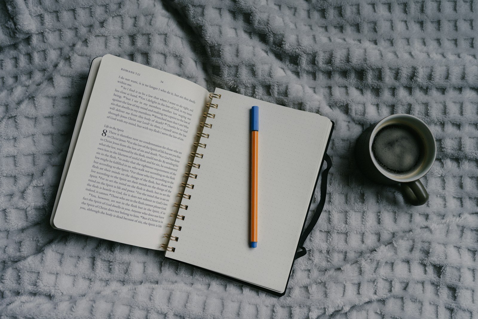 An open book, notebook, pen, and coffee cup arranged on a soft blanket