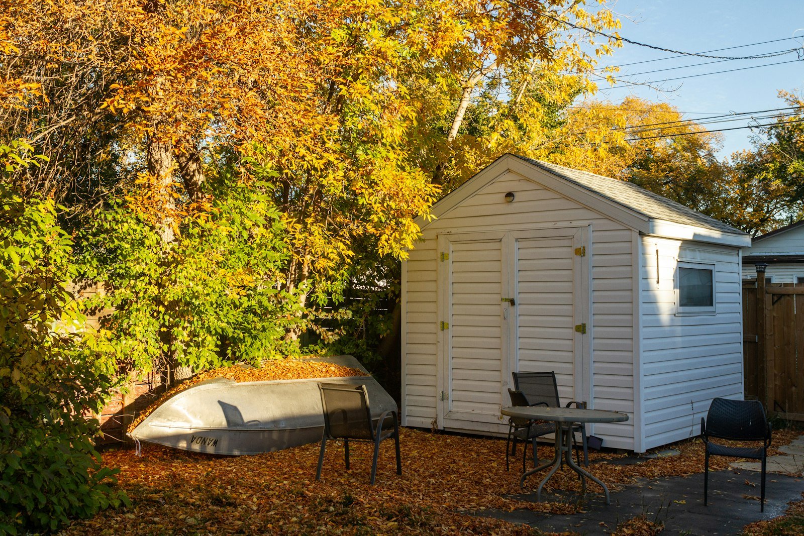 A small white shed structure in a backyard with a boat parked alongside it